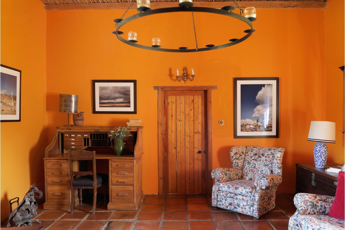 Indoor living space with orange walls and terracotta floors. An antique cabinet, vintage furniture, and wooden door.