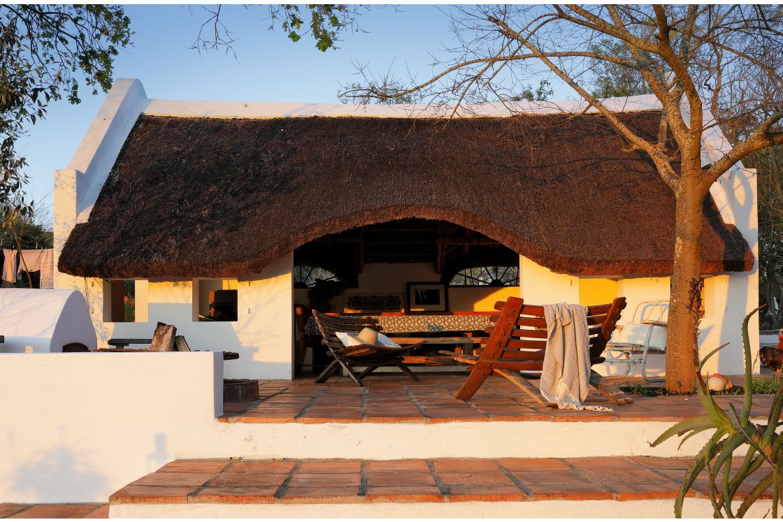 Thatch roof summer house with braai or outdoor fireplace, comfortable outdoor seating, and red-stone terrace.