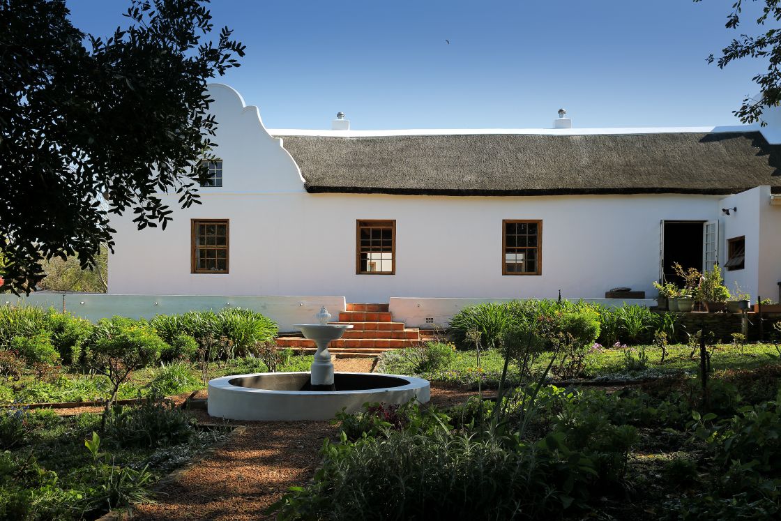 Garden with a central water feature and 4-way garden paths leading away, one of which ends in steps towards the main farmhouse.