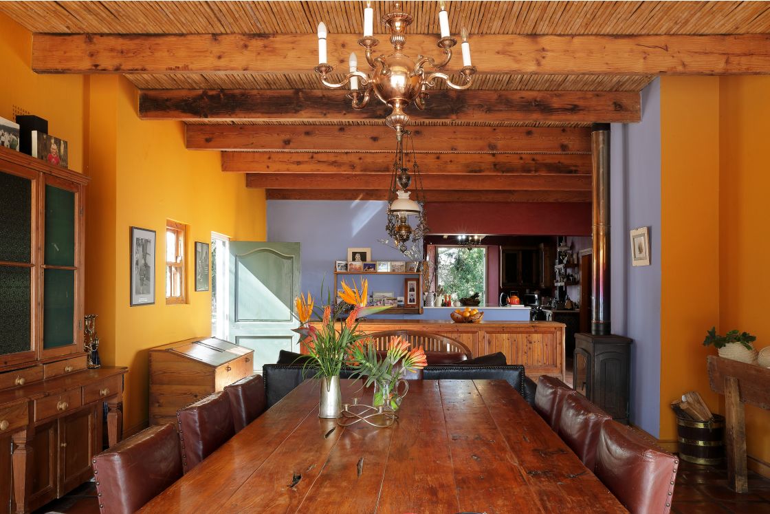 Large wooden table set with local flowers and leather chairs. Muted blue tones and orange walls compliment the space.