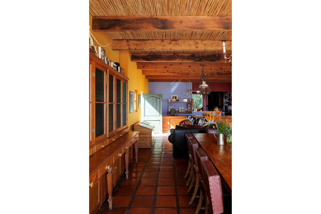 Living room view with leather chairs, wooden joinery, and terracotta floors. Blue and orange walls.