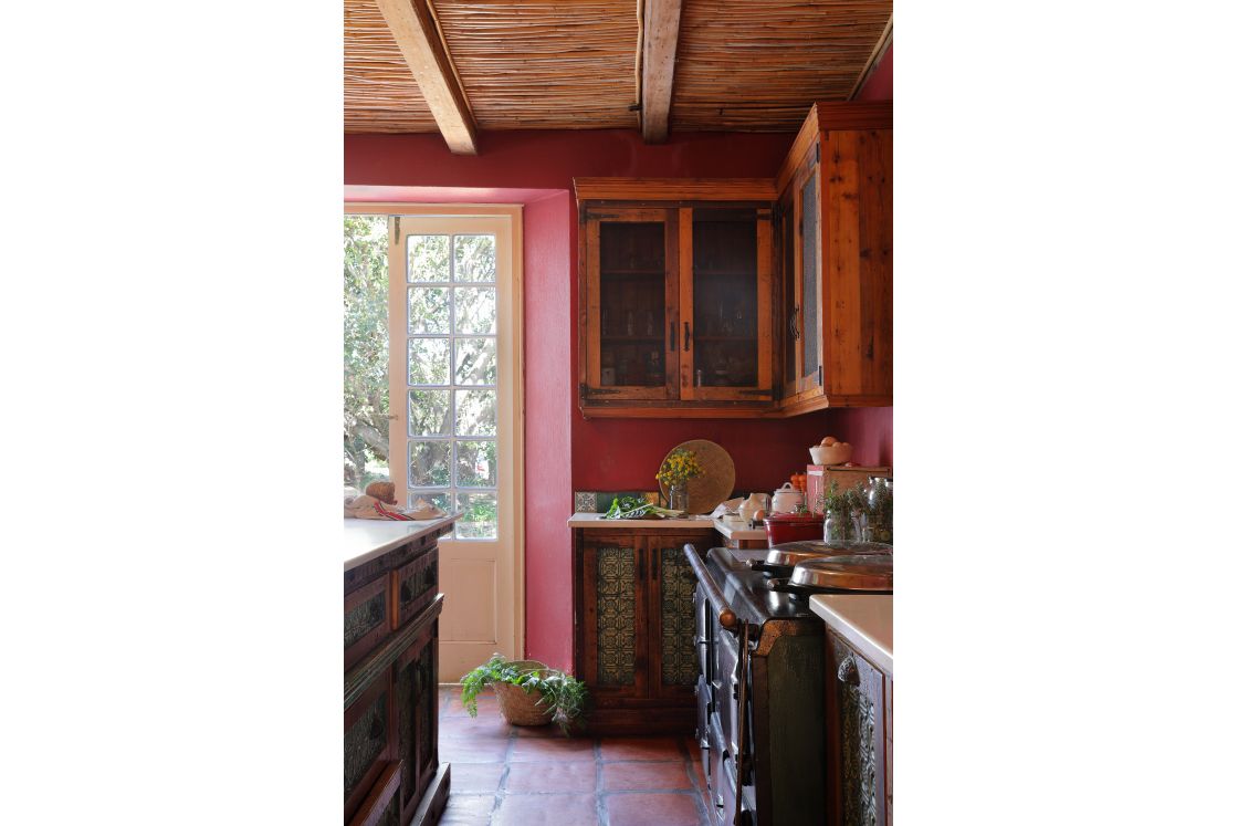 Kitchen with red walls, cupboards sit above refurbished countertops. A four-door Aga stove is set against the wall.