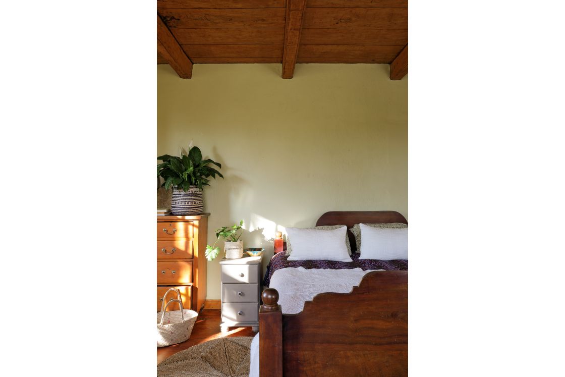 Large wooden bed and bedside table featured in the master bedroom of the main house, a woven rug covers the floor.