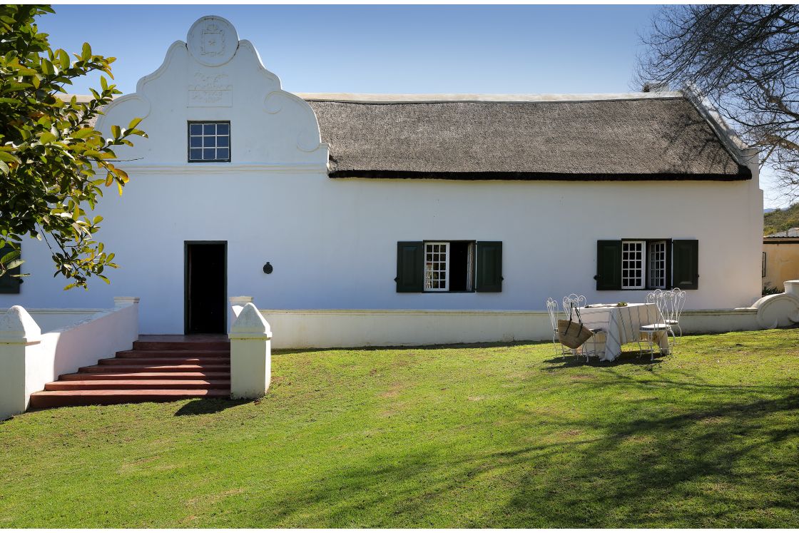 Table set for lunch in front of historic national-monument house. Dark green shutters and thatch roof.