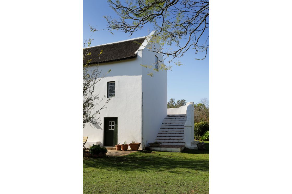 Historic national-monument house with green door and windows. Steps lead to the second floor of the building. Grass in the foreground.