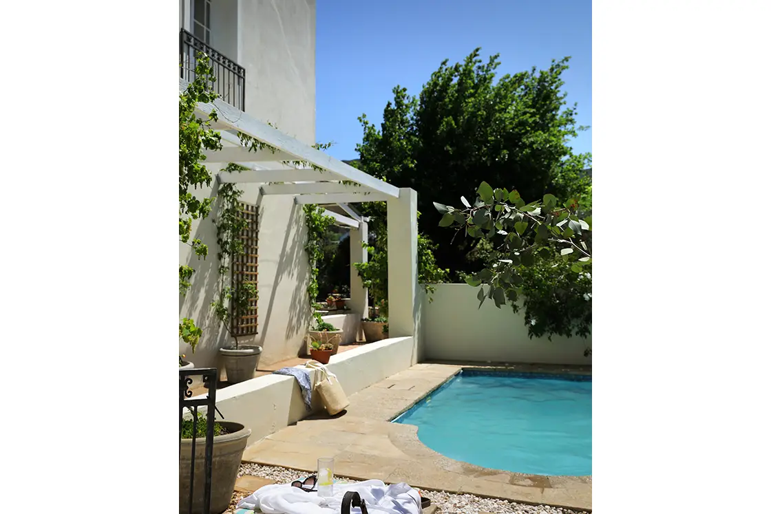 Perfect Hideaways real estate property: Outdoor area of heritage home featuring sun loungers and a swimming pool, an open-top pergola projects from the white house. The White House in Barrydale.