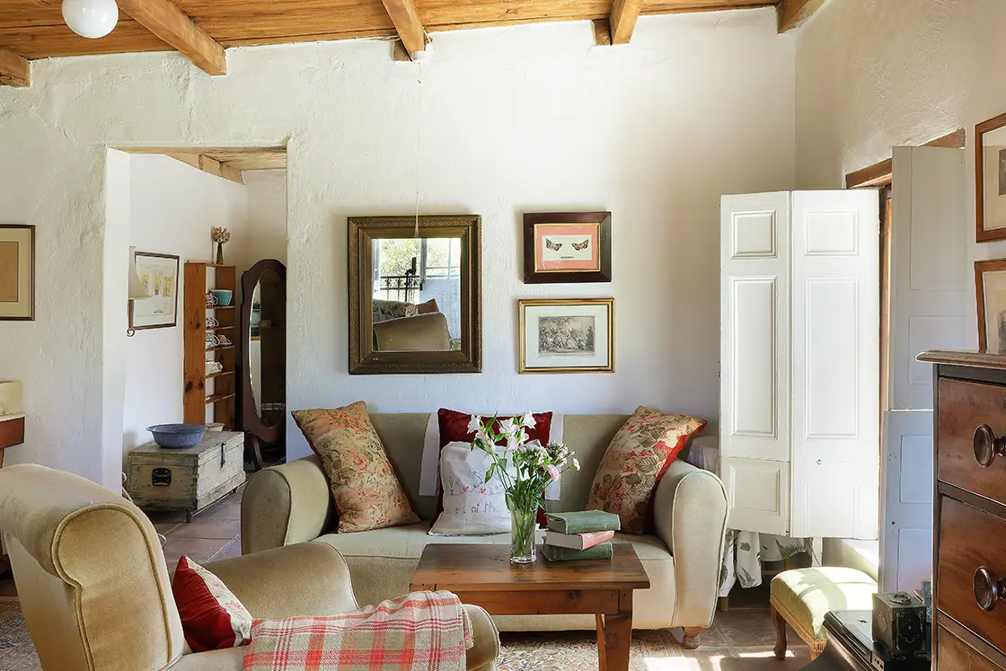 Perfect Hideaways real estate property: Wooden decor complements the muted tones of the couch with decorative cushions, a sloping wood ceiling, and white walls complete the refurbished heritage home. The White House in Barrydale.