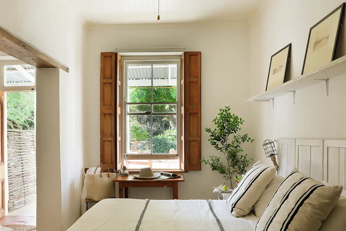 Perfect Hideaways real estate property: Neutral bedroom with wood accents in the window shutters, ceiling beams, and doorway. The White House in Barrydale.