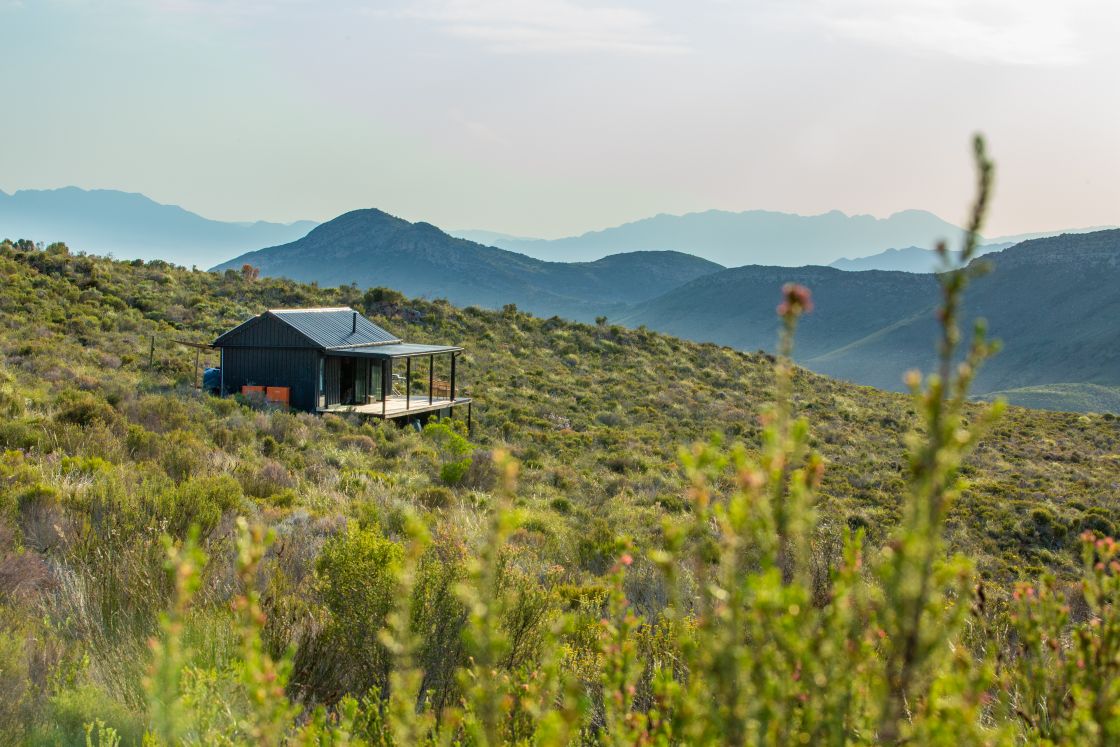 A lodge with a corrugated metal exterior and a shaded patio, featuring mountain peaks in the backgrounds, and hidden valleys below.