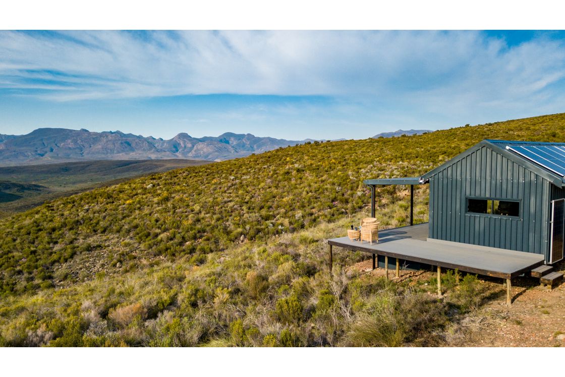 A quaint homestead with solar panels, featuring an outdoor patio with views of the surrounding expanse of mountain ranges.