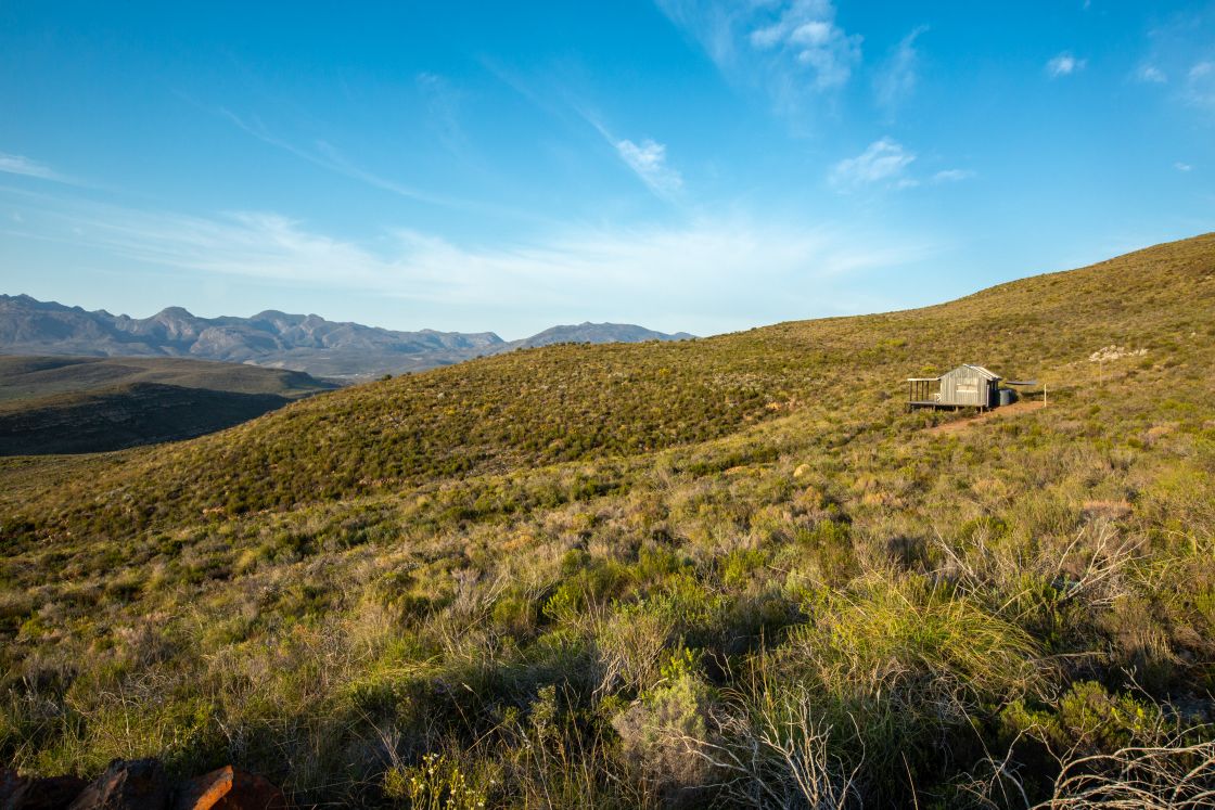 A secluded homestead on a plot of land for sale in the Western Cape, South Africa. The home is situated on a lush hillside in a mountainous region.