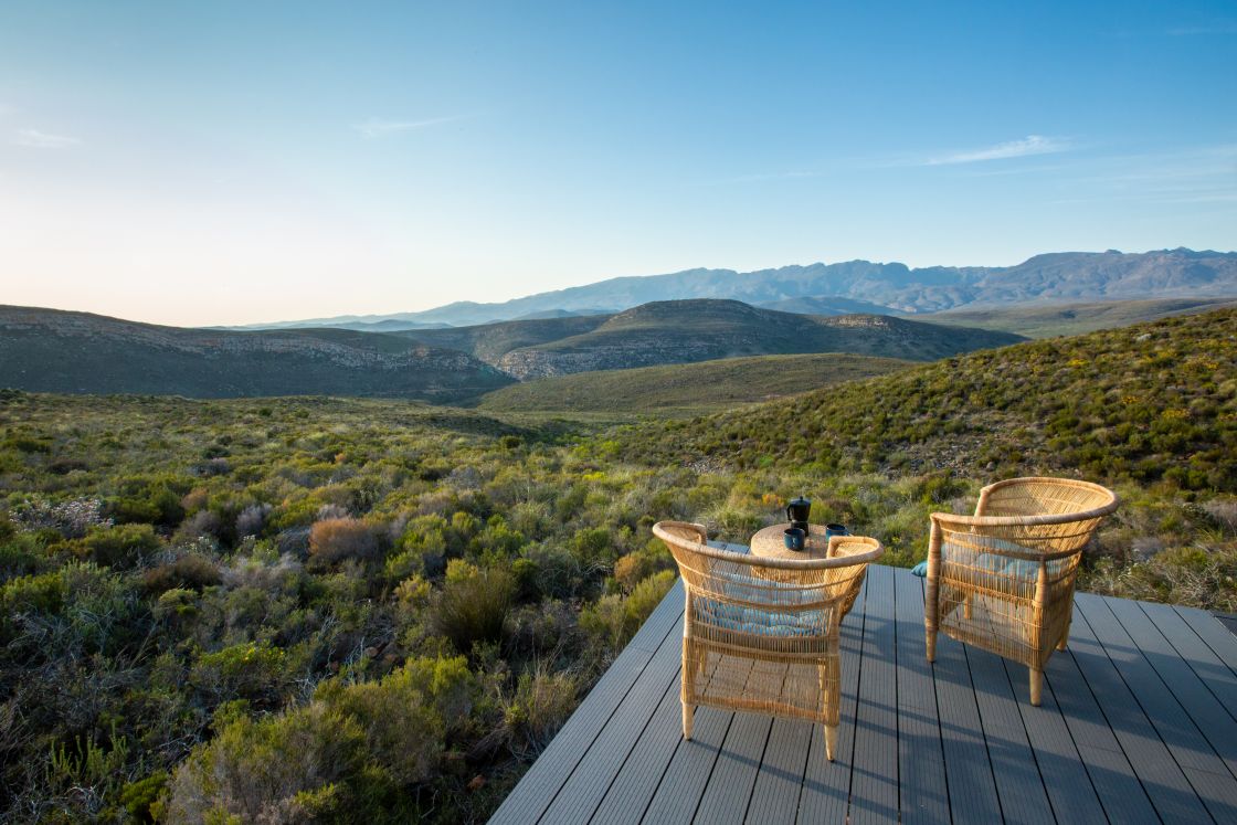 A corner of the homestead's patio with two wooden outdoor chairs, showcasing the expanse of the untouched mountains and mountain ranges of the Western Cape.