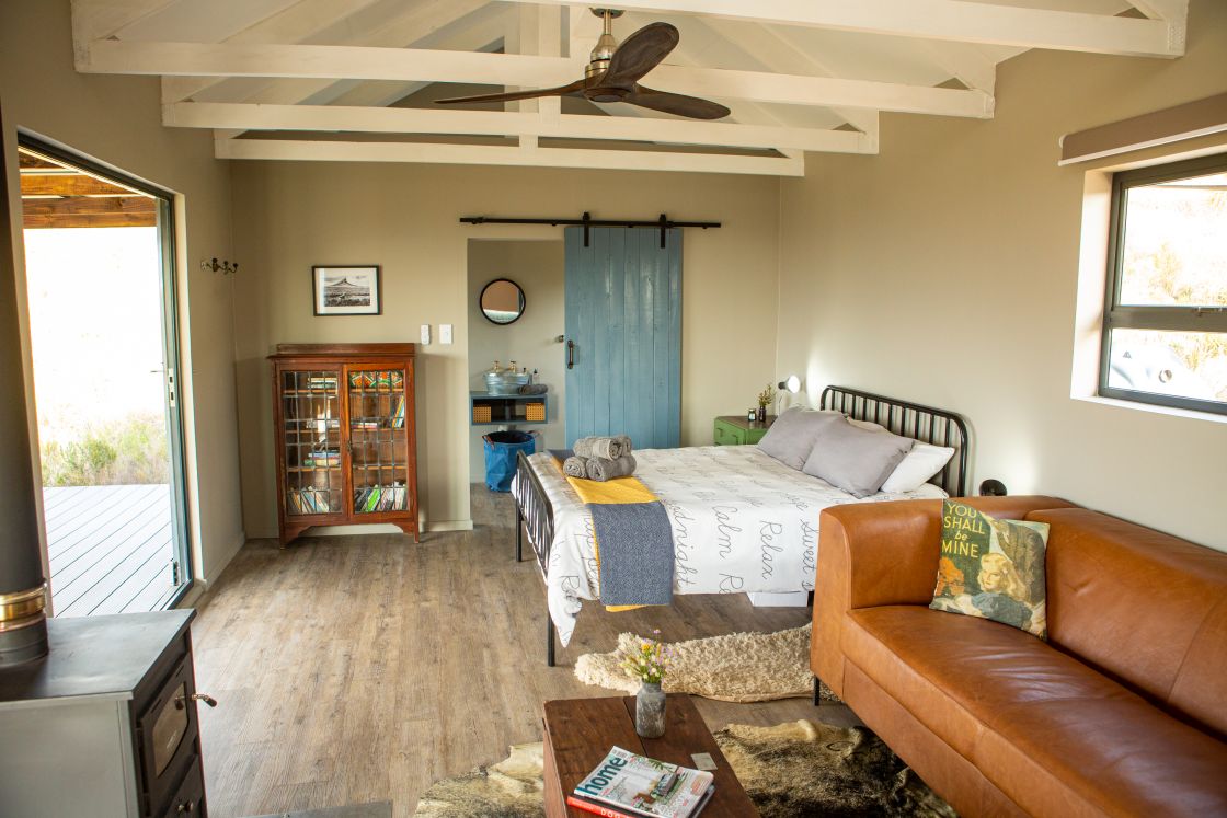 The living area of a small homestead, featuring a double bed with an en-suite bathroom, and a living area with an indoor fireplace and comfortable seating.