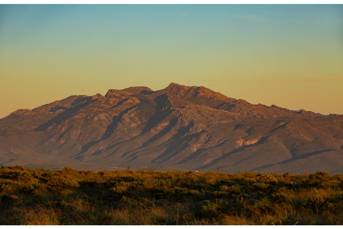 A lush hillside gives way to the distant valley at the foot of a striking range of mountain peaks and crevices.