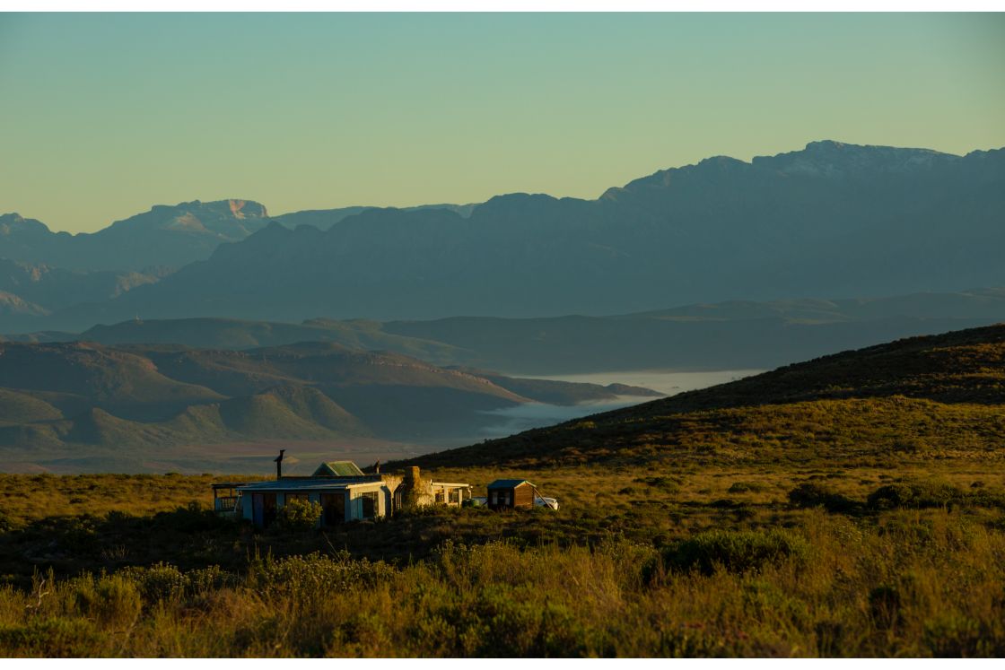 An eco-friendly homestead situated on a lush hillside surrounded by striking mountain ranges in the Overberg region of the Western Cape, South Africa.