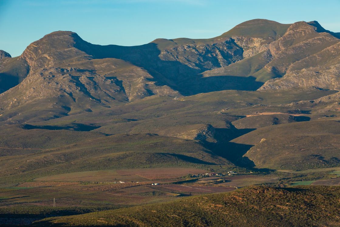 A plot of farmland containing a primary residence, as well as a handful of other buildings, situated at the foot of a striking mountain formation.