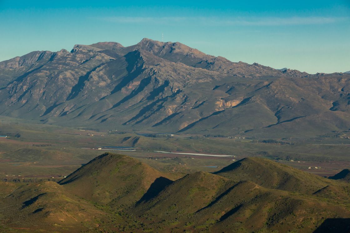 A landscape view of a valley with sparse farmland, situated between two substantial mountain formations.