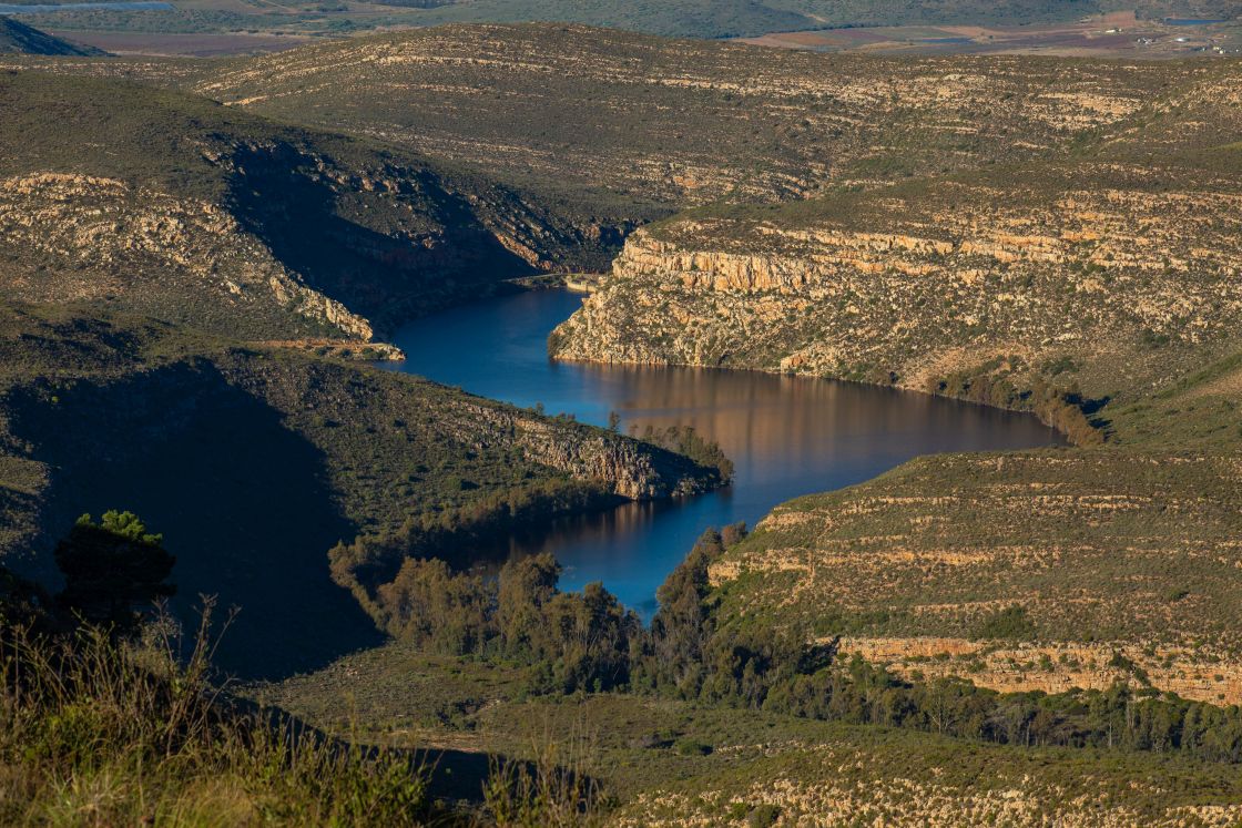 Rock formations form the bank of a winding river, surrounded by lush vegetation and farmland in the background.